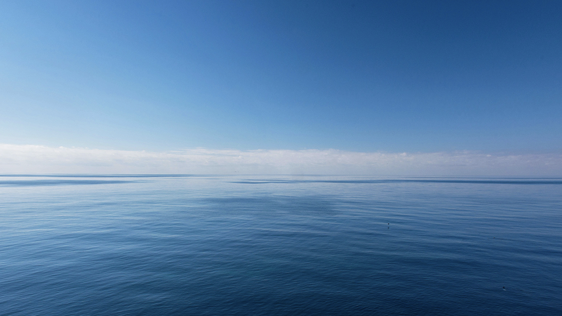 Photo of a calm sea with clouds above.