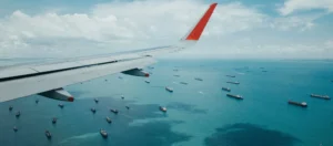View of airplane wing with sea and boats below