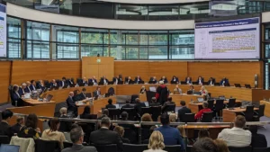 Image of ITLOS plenary, people in suits sitting in a circular room with wooden panelling, and a presentation projected onto a screen (not legible).