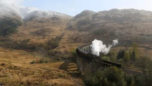 Steam train travelling across viaduct surrounded by mountains