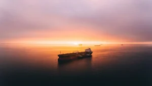 Photo of a large ship on a calm sea at sunset, with clouds in the sky.
