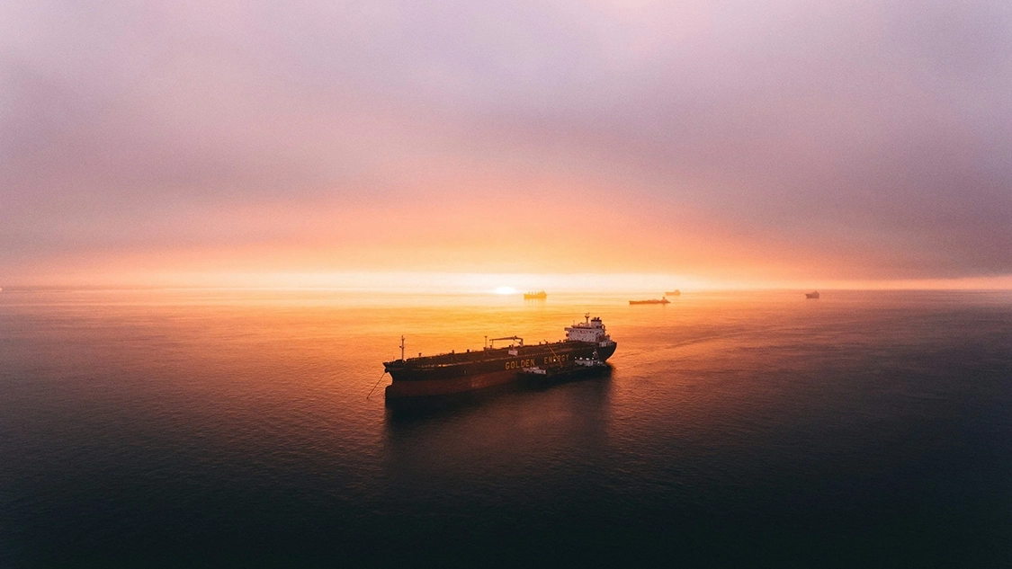 Photo of a large ship on a calm sea at sunset, with clouds in the sky.