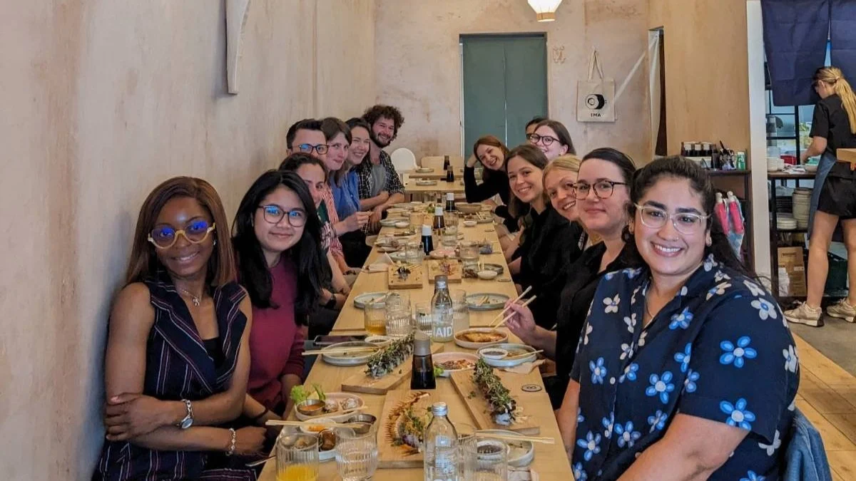 14 adults around a long brown table at a restaurant all smiling.