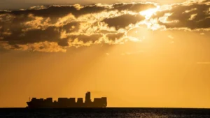 stock image of silhouette of a large hipping boat on the horizon in the distance with sunset in the background
