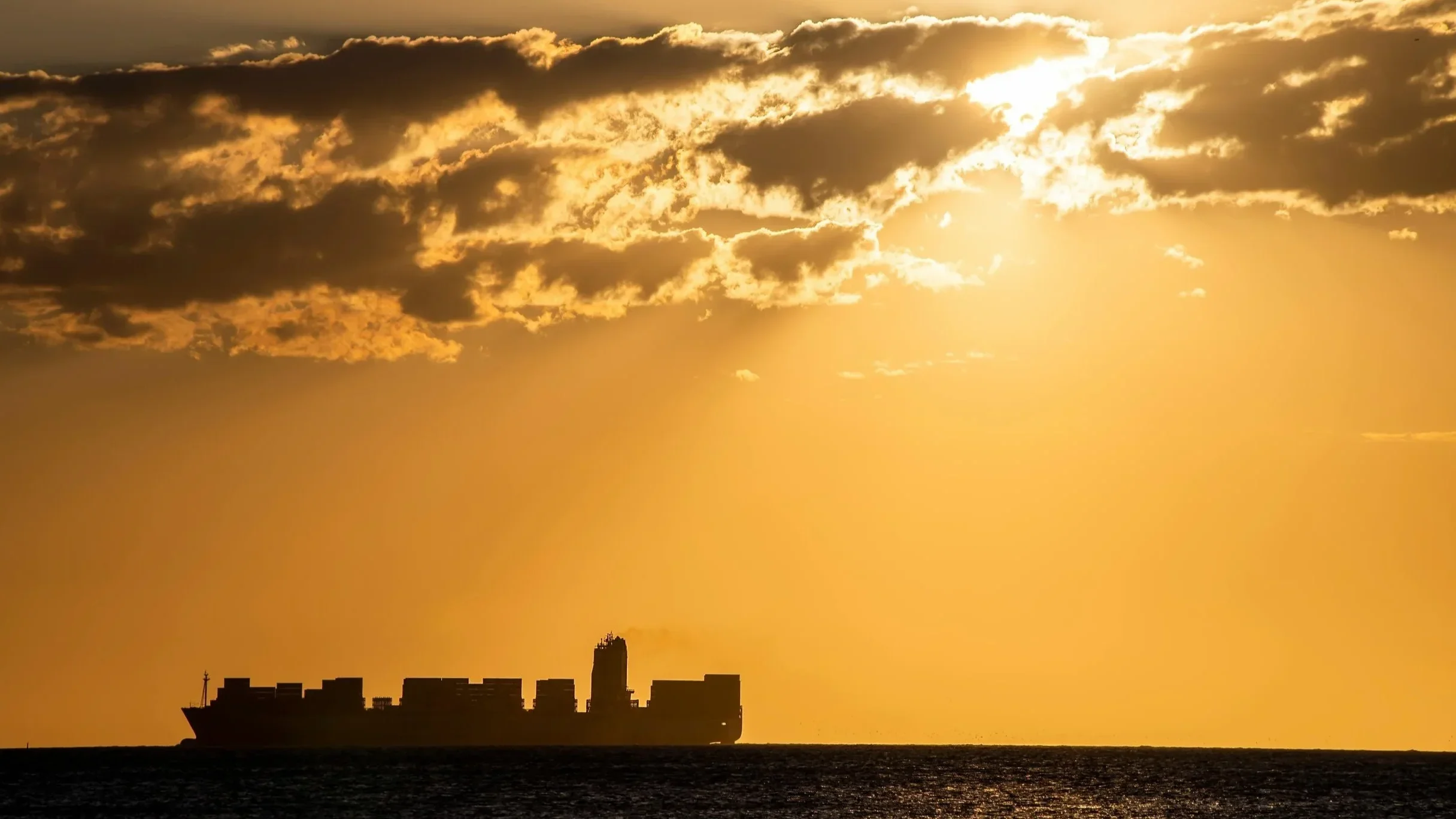 stock image of silhouette of a large hipping boat on the horizon in the distance with sunset in the background