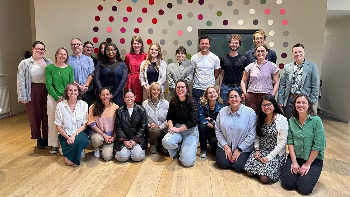 Photo of the Opportunity Green team, 23 staff members in total, some people kneeling, others standing. The floor is wooden and there is a spotted design on the wall behind them. Photo of the Opportunity Green team, 23 staff members in total, some people kneeling, others standing. The floor is wooden and there is a spotted design on the wall behind them.