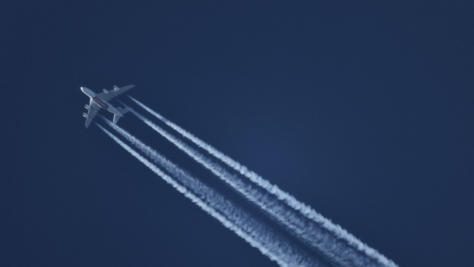 A jet plane with large contrails in its wake across the sky