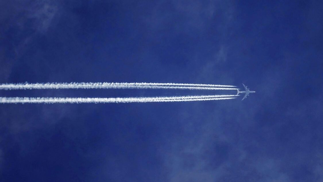 Aeroplane flying high above a deep blue sky leaving two thick white contrails behind it