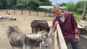 James smiling and leaning against a fence beside two donkeys