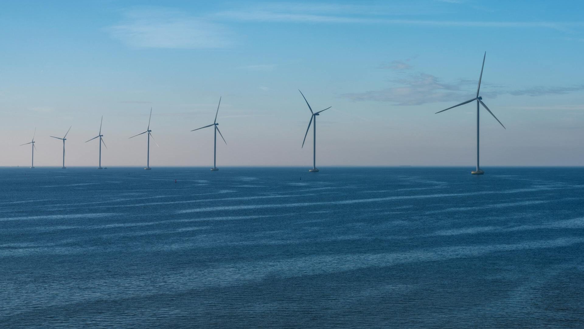 Row of wind turbines in the ocean with a blue and pink sky