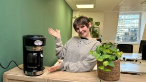 Our Legal Manager, Suki. wearing a grey top proudly presenting Opportunity Green's new coffee machine